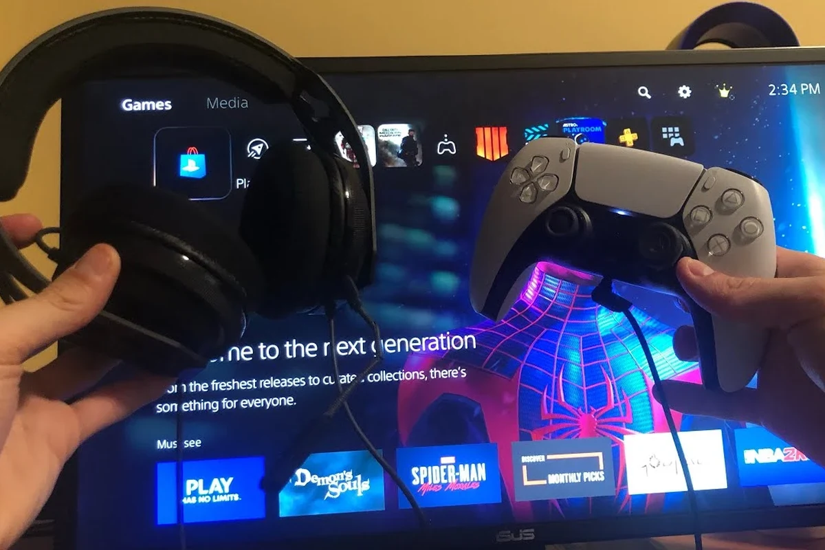 Person connecting wired headphones to a PS5 controller beside a gaming console setup