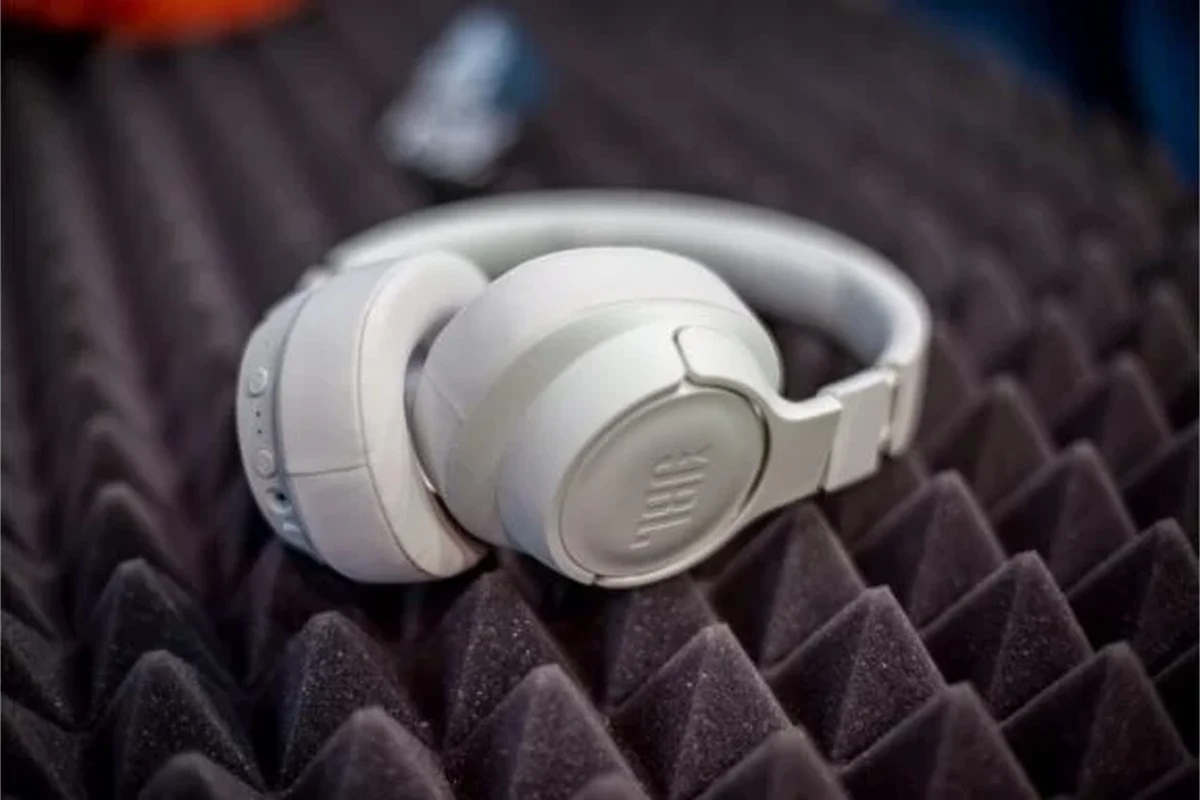 JBL wireless headphones pausing on a desk beside a smartphone and Bluetooth settings screen