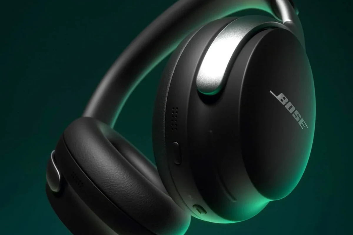Bose headphones being powered off on a desk beside a phone and charging case