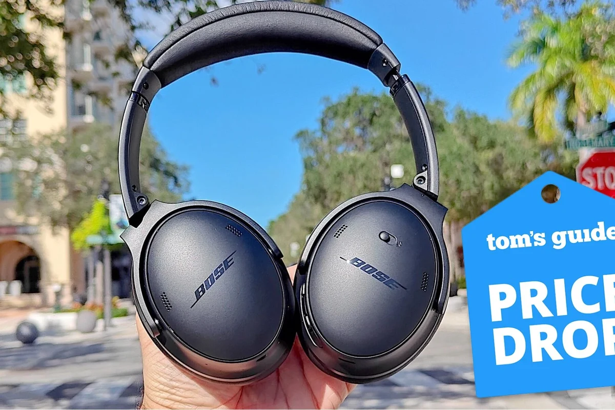 Bose headphones being powered off on a desk beside a phone and charging case