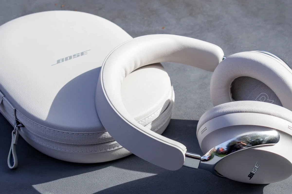 Bose QC Ultra headphones on a desk with phone, laptop, and travel case