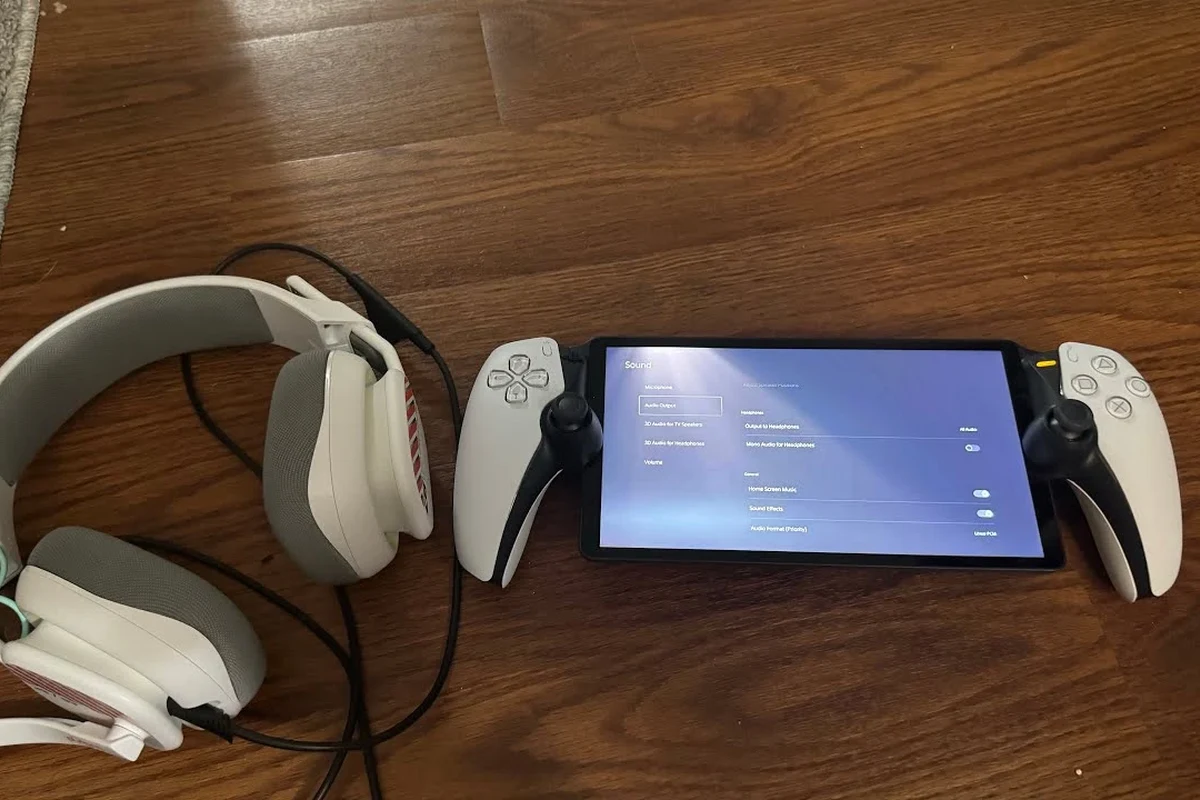 PlayStation Portal handheld gaming device with compatible headphones nearby on a desk