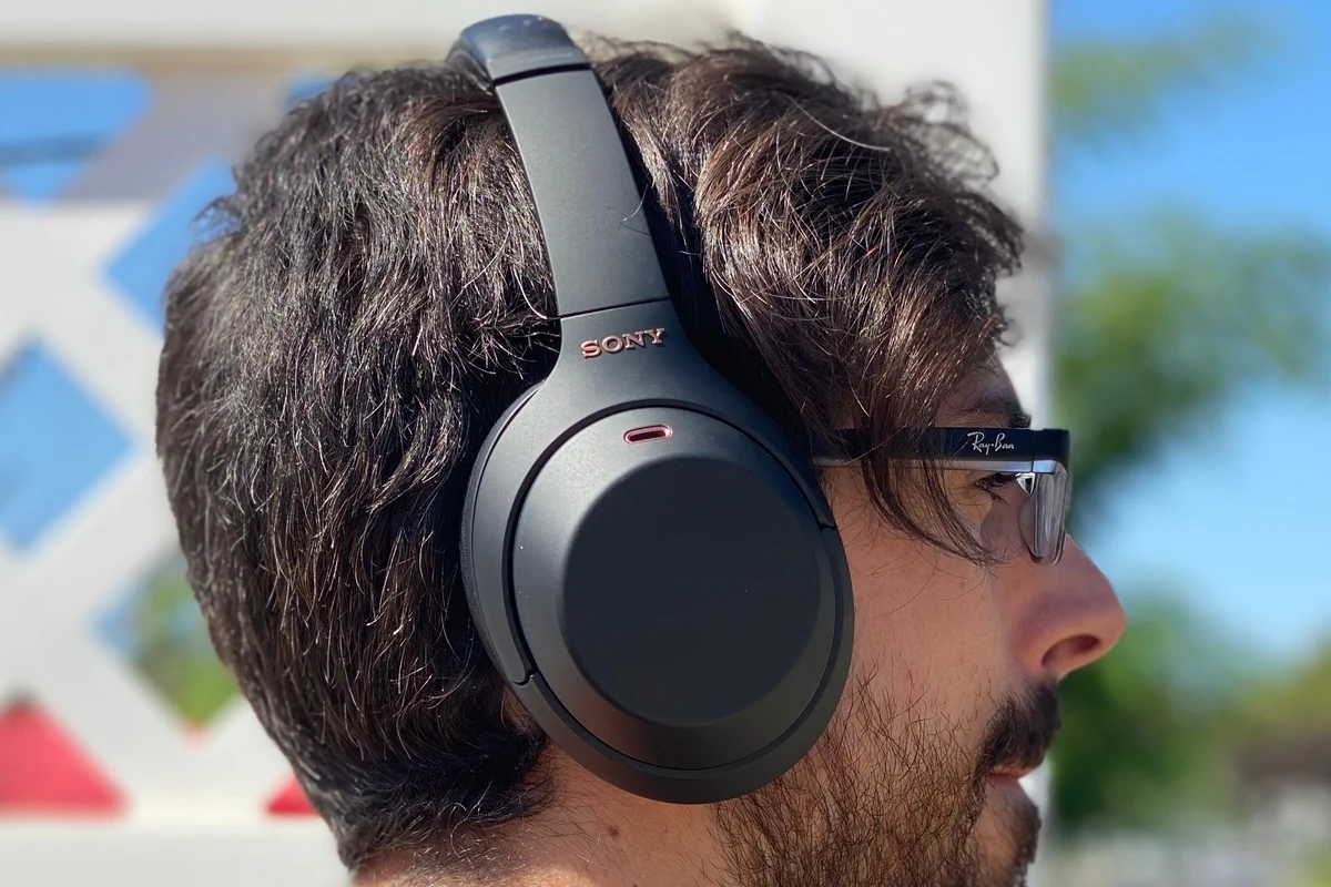 Sony WH-1000XM4 over-ear wireless headphones on a desk with phone and charging cable